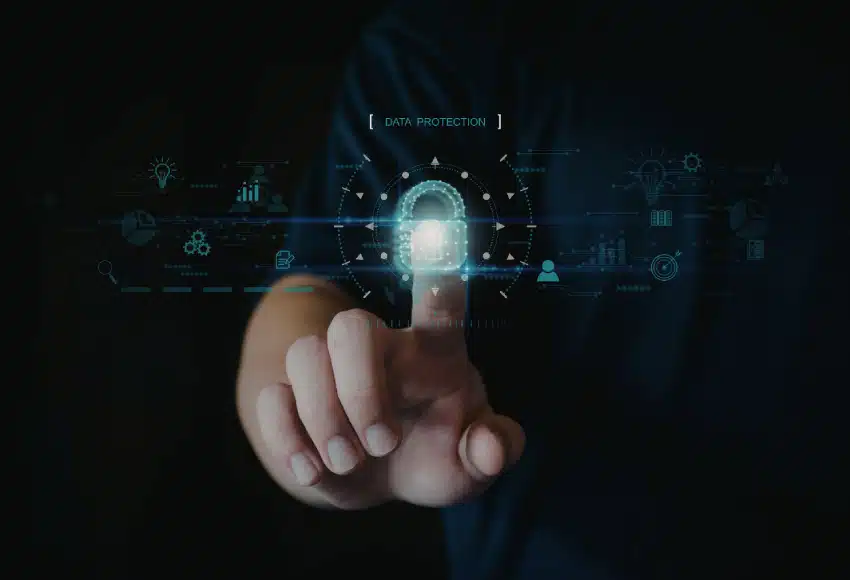 A person’s hand presses a virtual lock icon labeled “Data Protection” on a touchscreen, surrounded by digital security and technology graphics on a dark background.